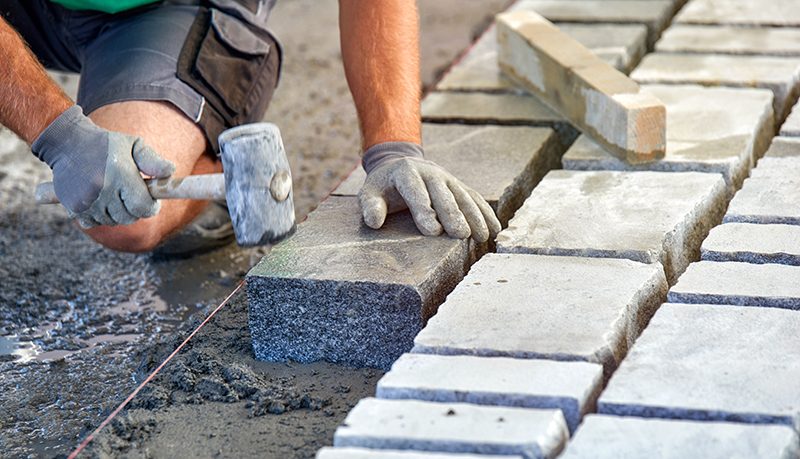 a workman's gloved hands use a hammer to place stone pavers. wor